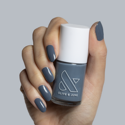 Hand holding Olive and June Favorite Beanie gel polish bottle with matching slate grey manicure nails