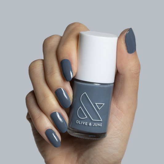 Hand holding Olive and June Favorite Beanie gel polish bottle with matching slate grey manicure nails
