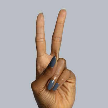 Hand with warm brown skin tone showing glossy Favorite Beanie gel polish manicure in moody slate grey against grey background