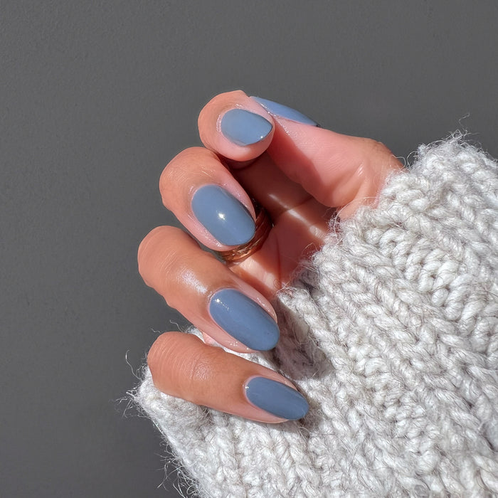 Hand wearing cozy knit sleeve with neatly done Favorite Beanie gel polish manicure in soft slate grey shade