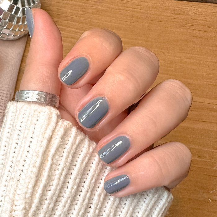 Hand with light skin tone wearing Favorite Beanie gel polish manicure in moody slate grey on cozy sweater background