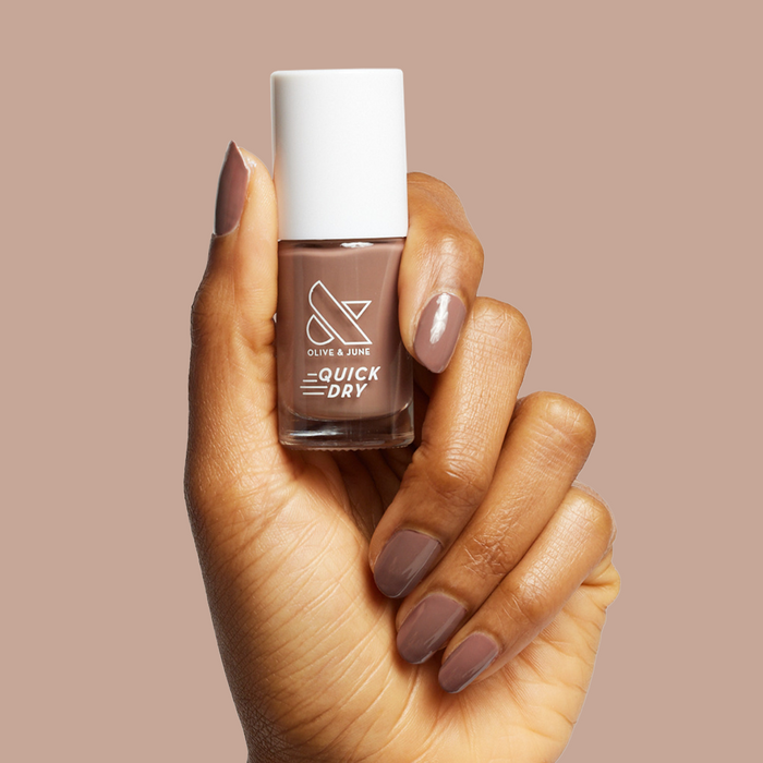 Hand holding Olive and June Fawn quick dry polish with matching neutral brown gel polish manicure