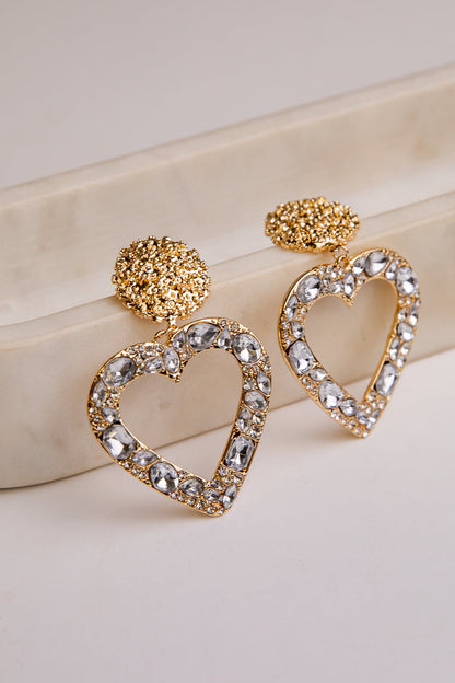 Heart-shaped earrings with gold and crystal details on a beige surface
