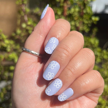 Floral Doodle | Short | Round - Tab Press-On nails in pastel blue with white flower doodles on hand outdoors in sunlight