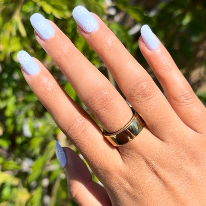 Floral Doodle | Short | Round - Tab Press-On nails with pastel blue base and white flower outlines on hand outdoors in sunlight
