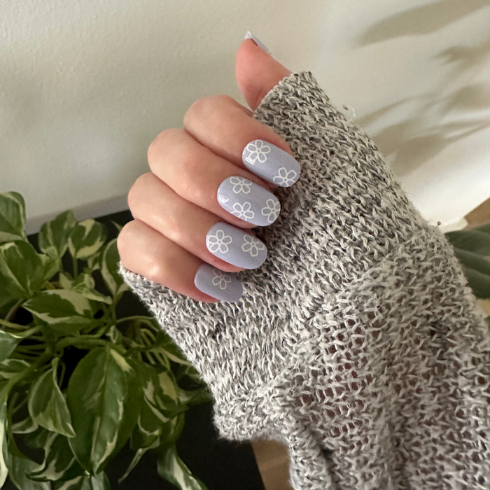Floral Doodle | Short | Round - Tab Press-On nails in pastel blue with white flower doodles shown on hand wearing cozy knit sweater indoors