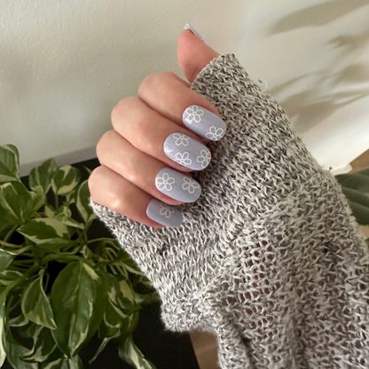 Floral Doodle | Short | Round - Tab Press-On nails in pastel blue with white flower doodles shown on hand wearing cozy knit sweater indoors