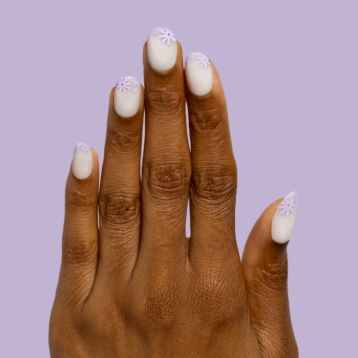 Floral Tip | Short | Round - Tab Press-On nails with soft neutral base and delicate lavender flowers at cuticle on hand against lavender background