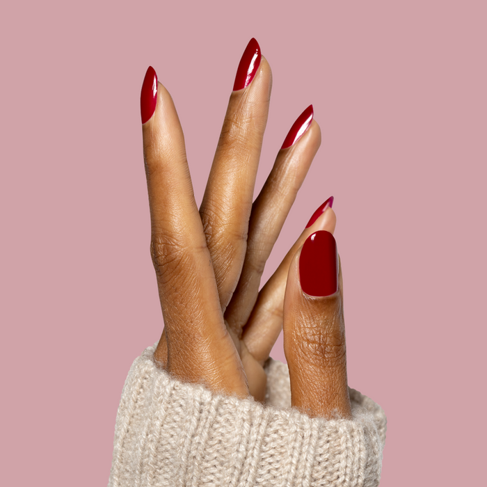 Hand with deep scarlet gel polish nails in almond shape wearing cozy knit cream sweater, featuring Garnet Glass mani