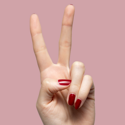 Hand showing two fingers with deep red Garnet Glass gel polish on short nails against muted mauve background