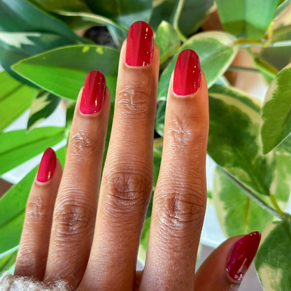 Fingers with medium-length nails painted in glossy Garnet Glass gel polish against green leafy background