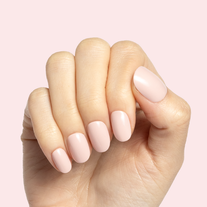 Gelato | Short | Round - Tab Press-On soft baby pink false nails on hand with smooth manicure finish on pale pink background