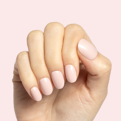 Gelato | Short | Round - Tab Press-On soft baby pink false nails on hand with smooth manicure finish on pale pink background