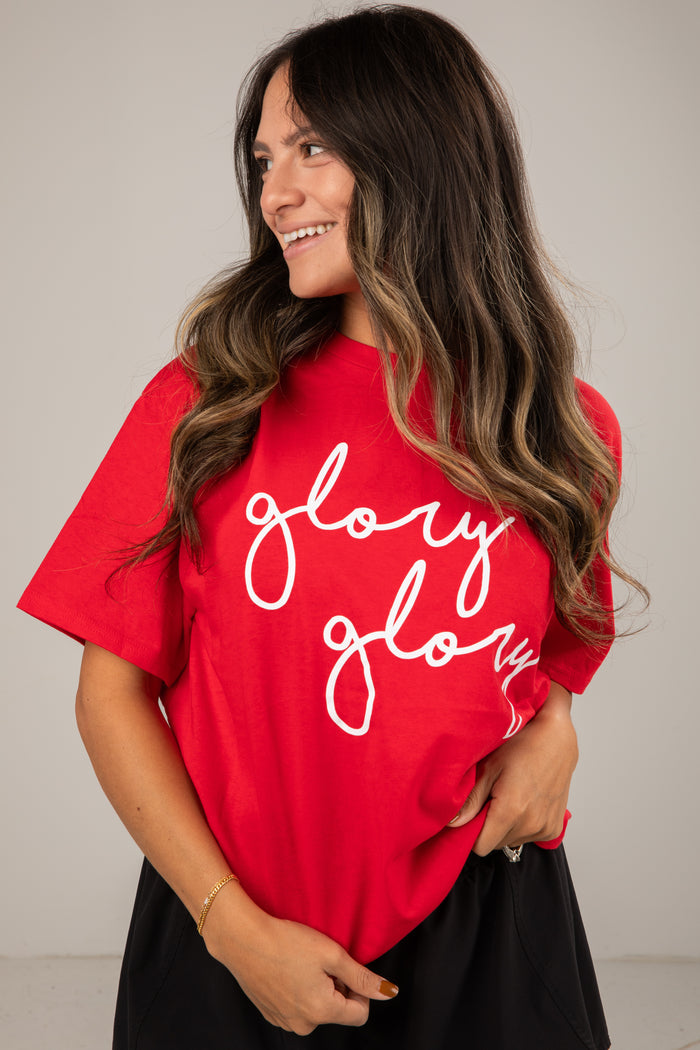 Woman wearing a red t-shirt with 'glory glory' text, smiling against a plain background