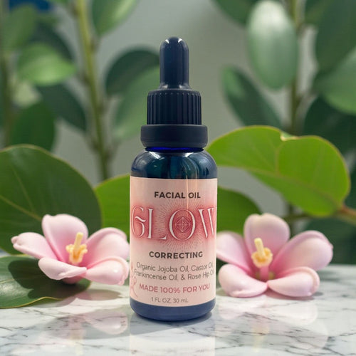 Facial oil bottle labeled 'GLOW' with pink flowers and green leaves in the background