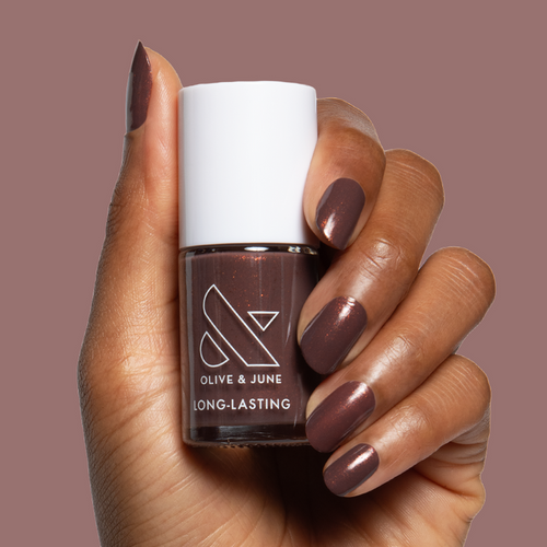 Hand with shimmer chocolatey neutral manicure holding Goal Getter long-lasting polish bottle against a mauve background