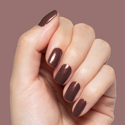 Hand with shimmering chocolatey brown manicure wearing Goal Getter long-lasting polish on muted mauve background