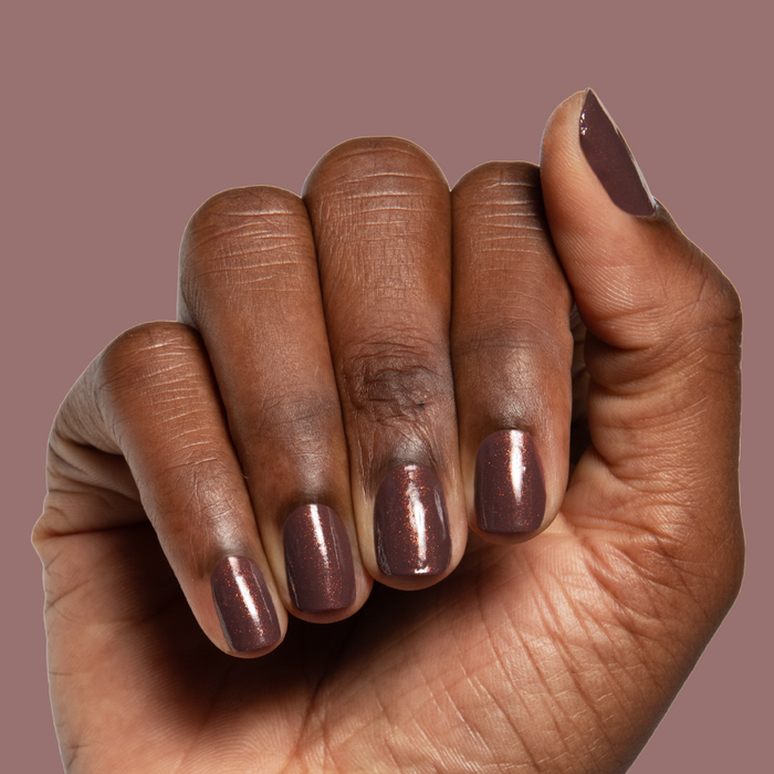 Hand with Goal Getter chocolatey shimmer gel polish manicure on a deep mauve background