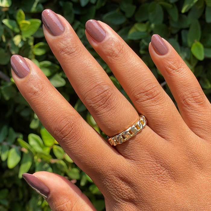 Hand with Goal Getter chocolatey neutral gel polish manicure featuring subtle golden shimmer against green foliage background