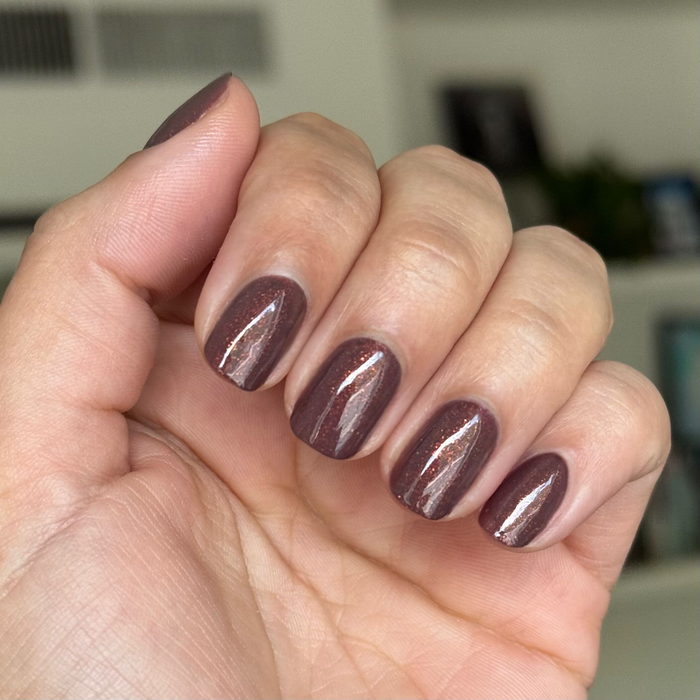 Close-up of hand with goal getter gel polish manicure in chocolatey brown with golden shimmer on neutral background