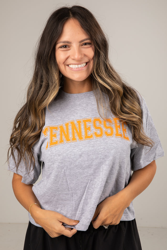 Woman wearing a gray t-shirt with 'TENNESSEE' printed in orange on a plain background