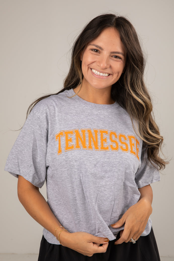 Woman wearing a gray t-shirt with 'TENNESSEE' printed in orange on a plain background