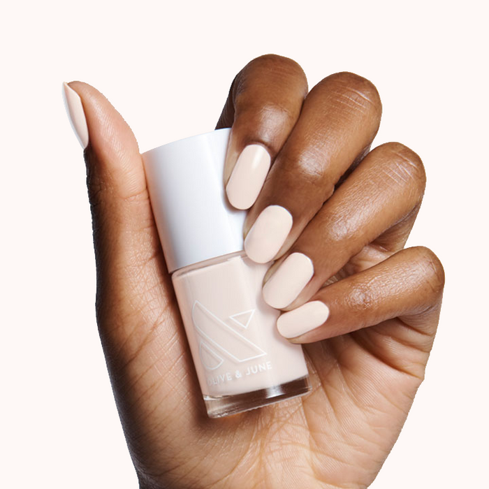 Hand holding HGC nail polish bottle with nails painted in a creamy toasted neutral shade for a warm classic mani