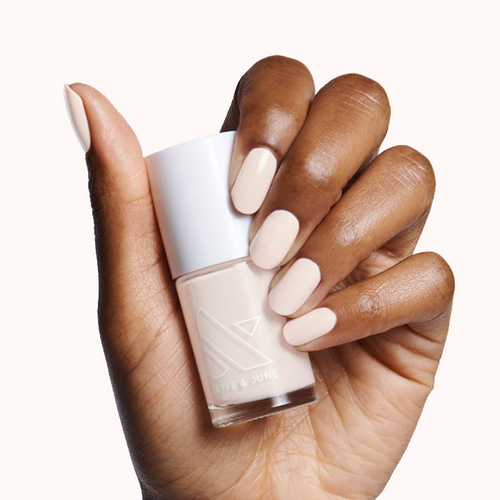 Hand holding HGC nail polish bottle with nails painted in a creamy toasted neutral shade for a warm classic mani