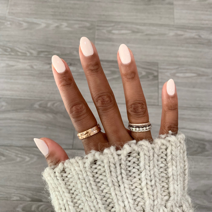 Hand with nails polished in HGC creamy toasted neutral shade wearing rings and a cozy knit sleeve for a warm mani look