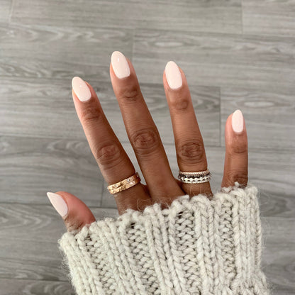 Hand with nails polished in HGC creamy toasted neutral shade wearing rings and a cozy knit sleeve for a warm mani look