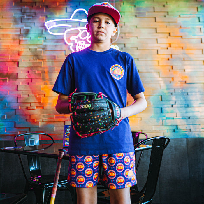 Child holding a baseball glove in front of a colorful brick wall with neon lights.
