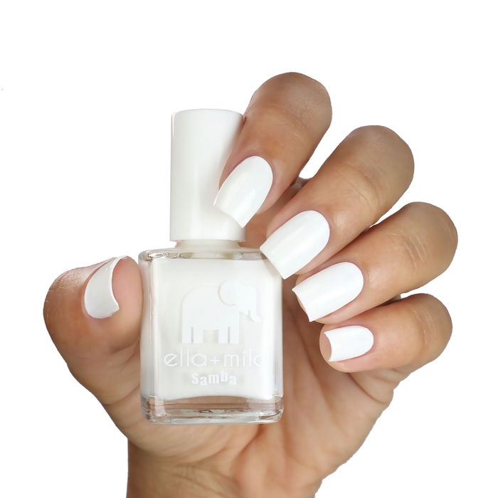 I Need a Tan white nail polish on a medium skin tone, hand holding the bottle