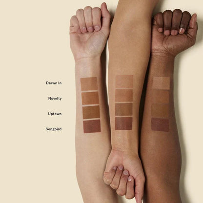 Swatch of ILIA Nightlite Bronzing Powder in Songbird showing warm, sun-kissed shades on arm, with product packaging visible.