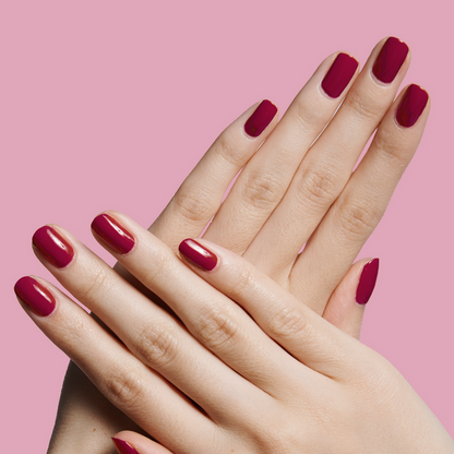 Hands with neatly manicured nails painted in JG rich berry polish against a soft pink backdrop