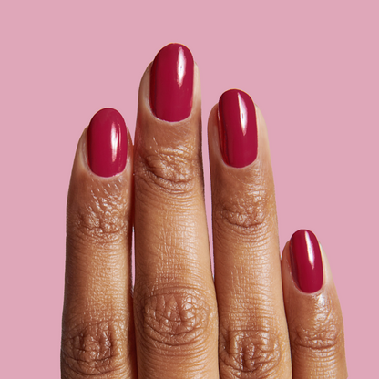 Close-up of hand with JG nail polish in rich berry shade on medium skin tone against pink background