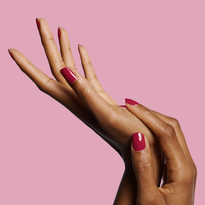 Hands with nails painted in JG rich berry polish showing a smooth and glossy mani against a soft pink background
