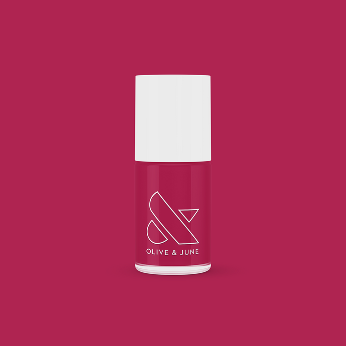 Bottle of JG nail polish in a rich berry shade with white cap against a matching berry-colored background