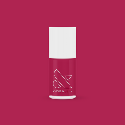 Bottle of JG nail polish in a rich berry shade with white cap against a matching berry-colored background