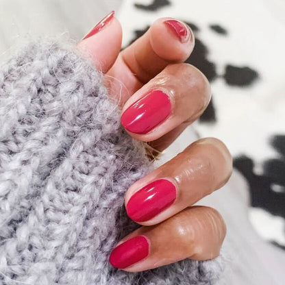 Close-up of hand with nails painted in glossy JG polish showing a rich berry manicure with cozy gray knit background