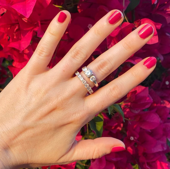Hand with nails painted in glossy JG polish in vibrant berry shade worn with silver rings against bright floral background