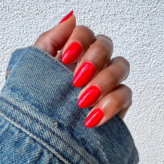 Hand with almond-shaped nails painted in bright red Kiss Cam polish for a shiny, long-lasting at-home manicure look