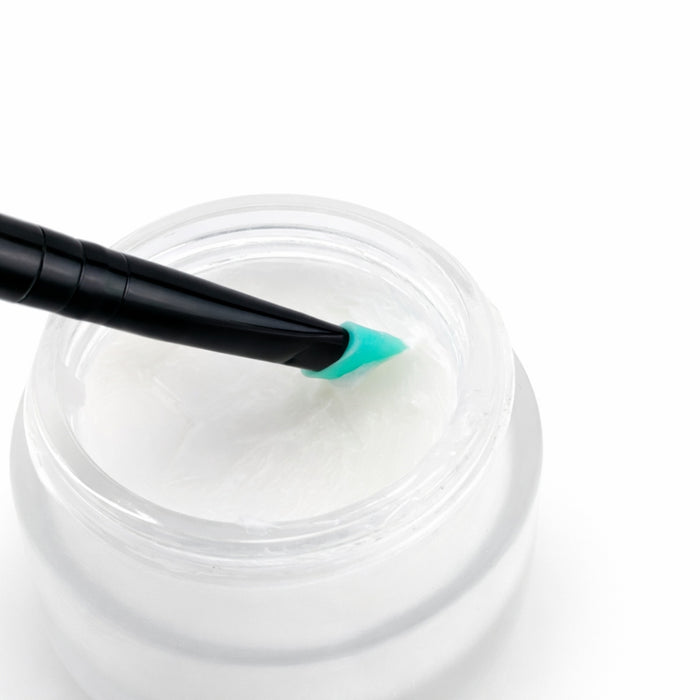 Jar of white lift & lami balm with a black and green applicator on a white background