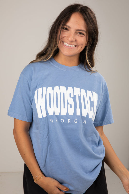 Woman wearing a blue t-shirt with 'Woodstock Georgia' text on a plain background