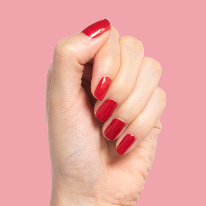 Hand showing nails painted with Lippy bold red shimmer polish against a soft pink background