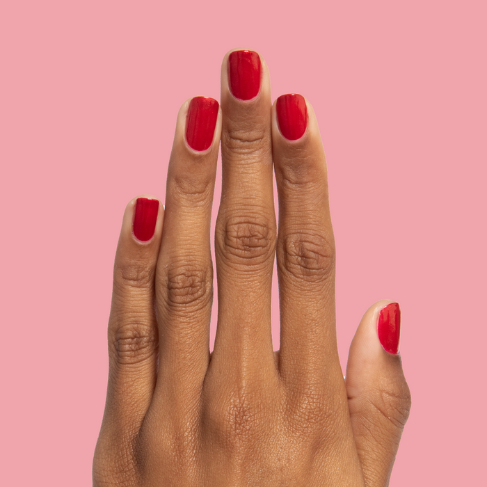 Hand with nails painted in glossy red shimmer Lippy polish for a bold at-home manicure by Olive and June
