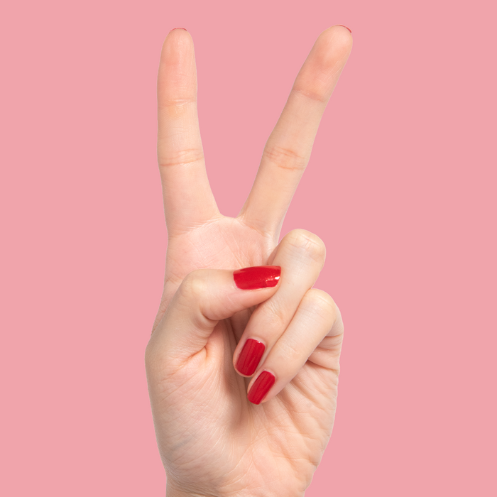 Hand showing nails painted with glossy red shimmer Lippy polish against a soft pink background for at-home mani
