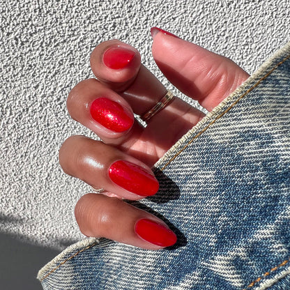 Hand with nails polished in vibrant glossy red shimmer Lippy polish holding denim fabric edge in sunlight