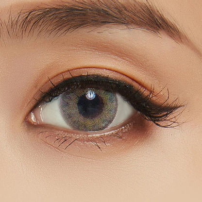 A close-up of a person's eye wearing NEO Vision Cosmo Green circle lenses by NEO Vision, with long eyelashes, a neatly groomed eyebrow, and subtle eyelid makeup.
