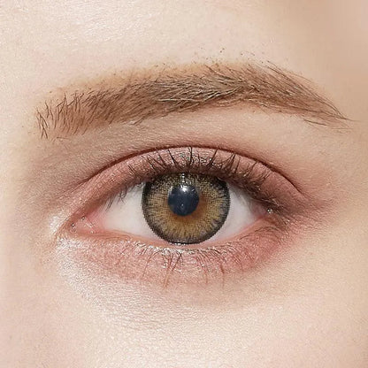 A close-up of a human eye with fair skin and natural makeup wearing NEO Vision Cosmo Grey lenses by NEO Vision, highlighting the subtle effect of these coloured contacts alongside groomed eyebrows and light brown-green eye tones.