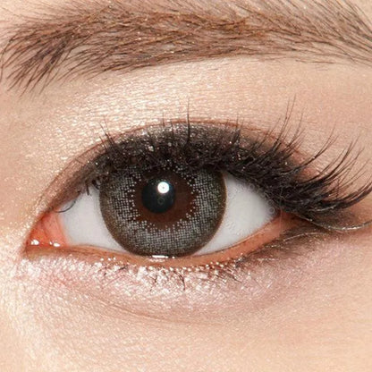 A close-up of an eye with brown irises wearing NEO Vision Extra Dali Grey lenses by NEO Vision, featuring long curled lashes and shimmery eyeshadow.